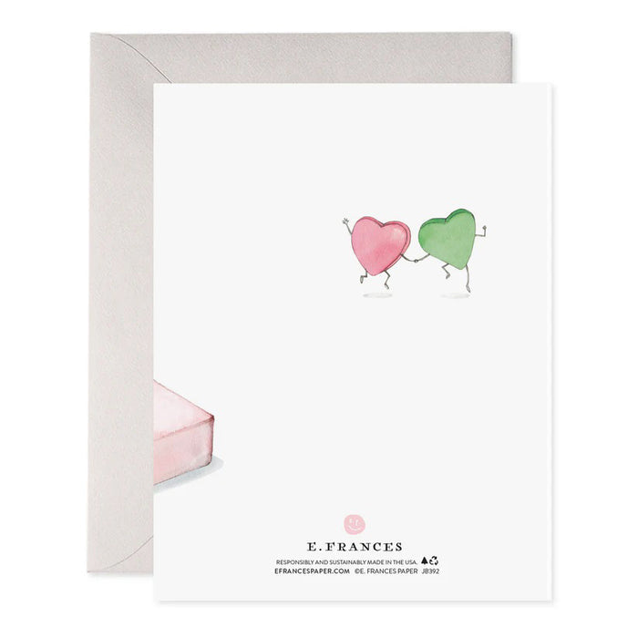 The "We Gotta Get Out More" greeting card by E. Frances Paper showcases a pink "SWEET HEARTS" candy box with two heart-shaped candies stepping out. Crafted on luxe heavyweight paper, it features the playful text above and gold foil elegance beneath with "HAPPY VALENTINE'S DAY.