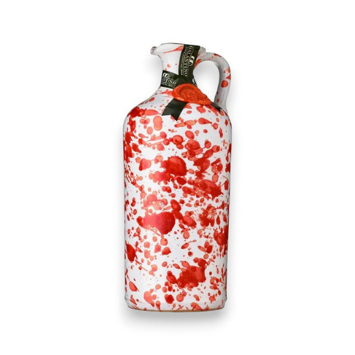 A white ceramic bottle with a handle, adorned with red paint splatters and a green neck label, stands on a white background—ideal for presenting Zia Pia Imports’ Gallantino Extra Virgin Olive Oil.