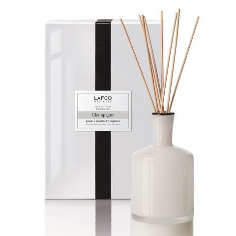 A LAFCO CHAMPAGNE, PENTHOUSE DIFFUSER with slim wooden reeds is displayed before its white box, evoking fresh grapefruit and sparkling bubbly notes.