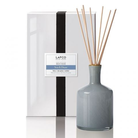 A gray glass diffuser with natural reeds sits before a white LAFCO Sea & Dune Beach House Diffuser box, featuring a black ribbon and silver label, evoking fresh coastal scents of sea grass and lily.