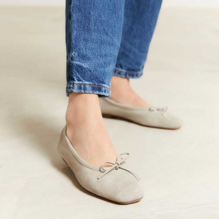 The REQINS - HARMONY BALLERINA FLATS by REQINS are shown in taupe suede with a small front bow and low heel, displayed in side profile against a plain light background.