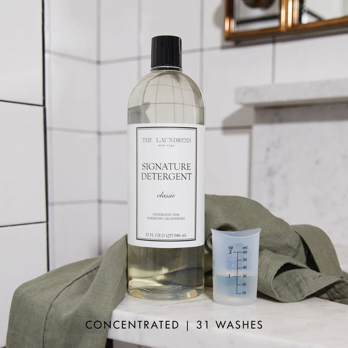 A 32 oz clear plastic bottle of THE LAUNDRESS - SIGNATURE DETERGENT, featuring a black cap and white label, designed for everyday laundry and effective stain removal.