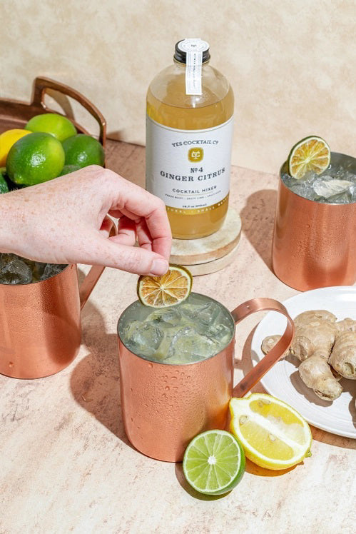 A clear glass 16 fl oz (473 ml) bottle of YES COCKTAIL CO - GINGER CITRUS COCKTAIL MIXER with a white label, green accents, and black text. The pale yellow mixer delivers a zesty ginger citrus kick—perfect for mule cocktails.
