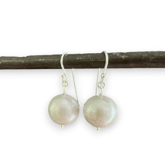 ANN LIGHTFOOT FRESHWATER PEARL DROP EARRINGS feature a single round white freshwater pearl on sterling silver earwires, shown hanging from a dark rod against a white background.