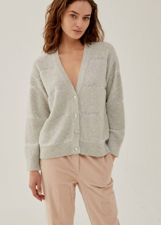 A woman with wavy brown hair models the ANNECLAIRE - PAILETTES STRIPE CARDIGAN, a light grey cotton piece with subtle horizontal stripes, paired with beige pants against a plain background.