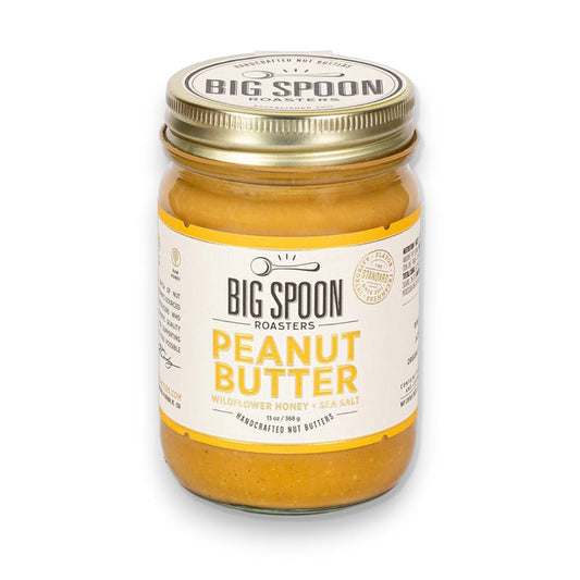 A glass jar of BIG SPOON ROASTERS Peanut Wildflower Honey Nut Butter, made with fresh-roasted peanuts, wildflower honey, and sea salt, featuring a gold lid and a white and yellow label.