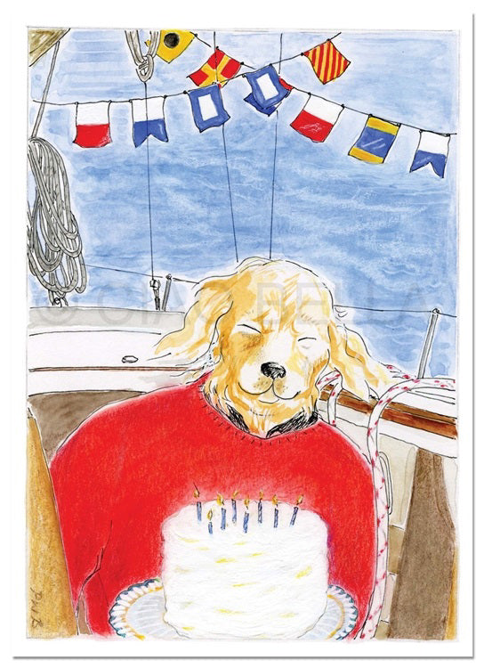 A golden retriever in a red sweater sits on a boat before a birthday cake, eyes closed. Nearby is CIAO BELLA's "ALL HANDS ON DECK CARD" by CIAO BELLA, with nautical flags overhead against the blue sky.