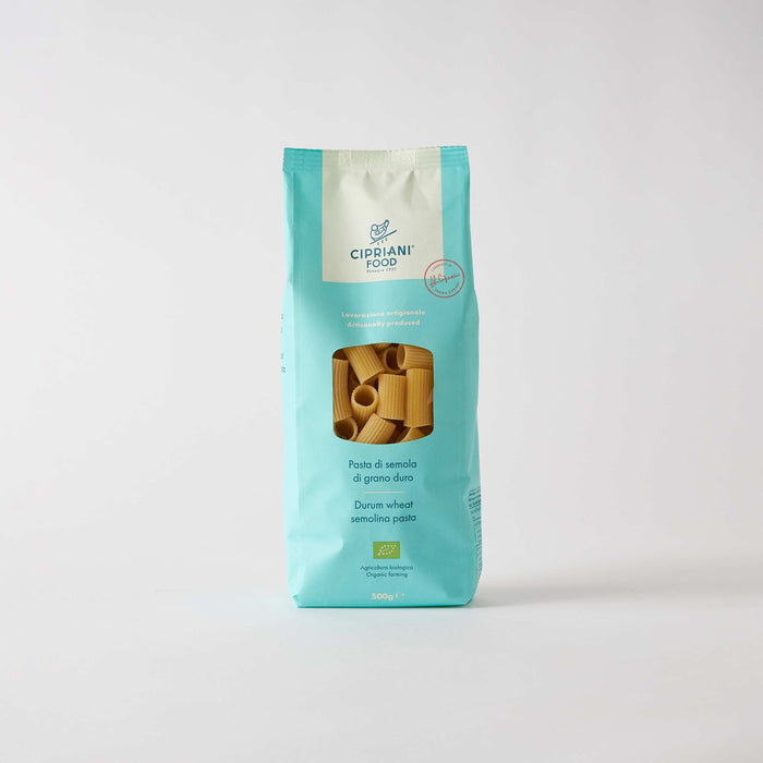 A turquoise and white CIPRIANI - ORGANIC RIGATONI PASTA package from ATALANTA CORPORATION stands upright on a white background, with a window showing rigatoni made from durum wheat semolina and Italian text on the front.