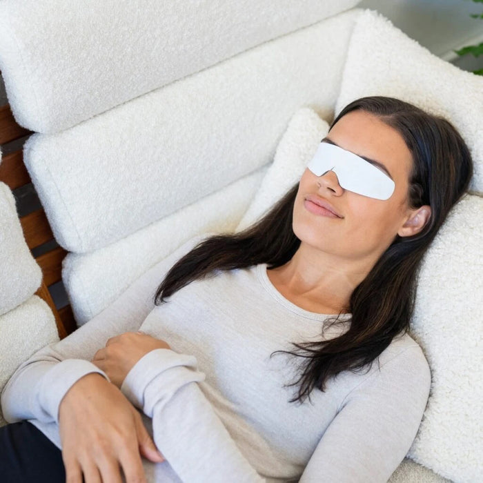 A white pouch with green designs reading "CORNEACARE - RESCUE SELF COOLING EYE MASK" by CORNEA CARE is shown next to a light blue, under-eye shaped mask. It offers soothing relief for eye care and dry eyes. The backdrop is plain white.