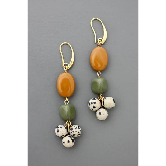 DAVID AUBREY JASPER SERPENTINE DALMATION CLUSTER EARRINGS by DAVID AUBREY feature gold-plated brass, an oval amber bead, a square green bead, and three small Dalmatian-spotted white beads against a gray background.