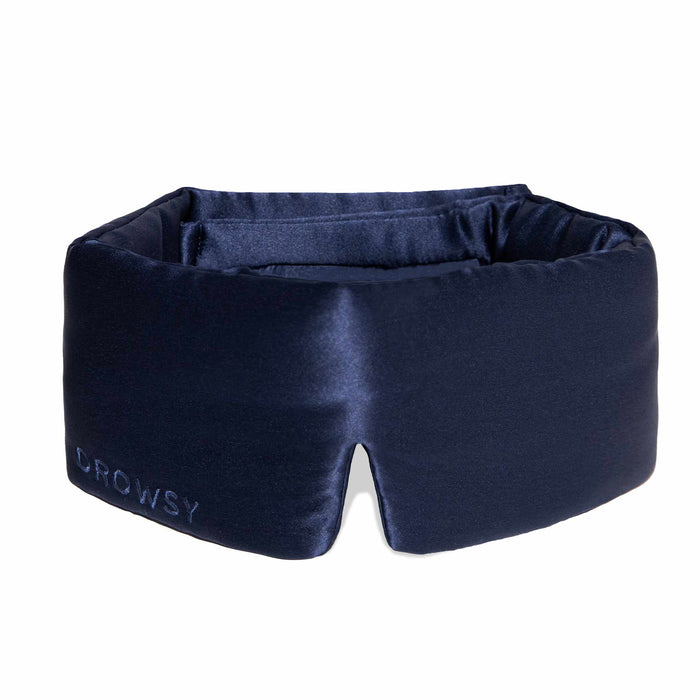 A person wearing a white tank top is lying on a pillow with the DROWSY - SATIN SLEEP MASK by DROWSY SLEEP CO covering their eyes. They look relaxed, enjoying beauty sleep as their hand rests gently on the pillow.