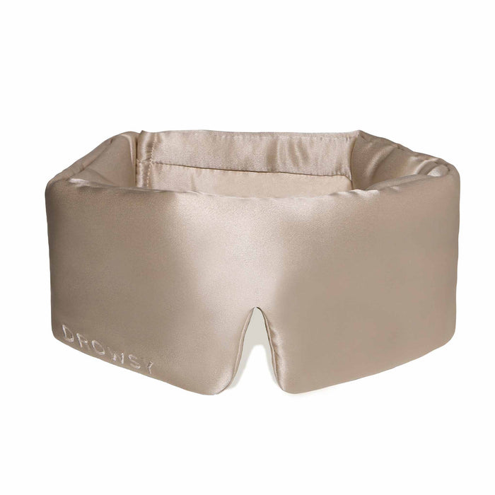 A person wearing a white tank top is lying on a pillow with the DROWSY - SATIN SLEEP MASK by DROWSY SLEEP CO covering their eyes. They look relaxed, enjoying beauty sleep as their hand rests gently on the pillow.