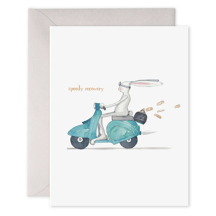 The E. FRANCES PAPER "Speedy Recovery" card features a rabbit in goggles on a teal scooter, leaving behind carrots, with "speedy recovery" printed in orange on luxe heavyweight paper. Adds charm to any wish!.