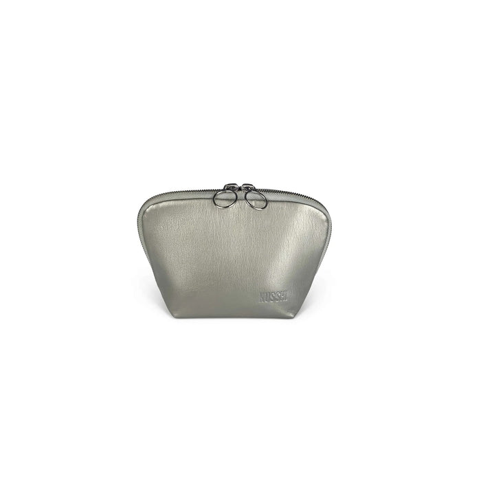 The KUSSHI EVERYDAY MAKEUP BAG IN VEGAN LEATHER is a small, metallic silver pouch with dual zipper pulls and subtle texture. "KUSSHI" is embossed on the corner. Perfect as a travel makeup organizer, it's shown against a white background.