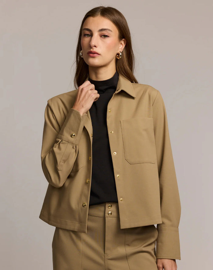 A woman with straight brown hair and gold hoop earrings is seen from the back in the HINSON WU ASTRID Long Sleeve Traveler's Twill Shirt Jacket, styled for travel, against a plain background.