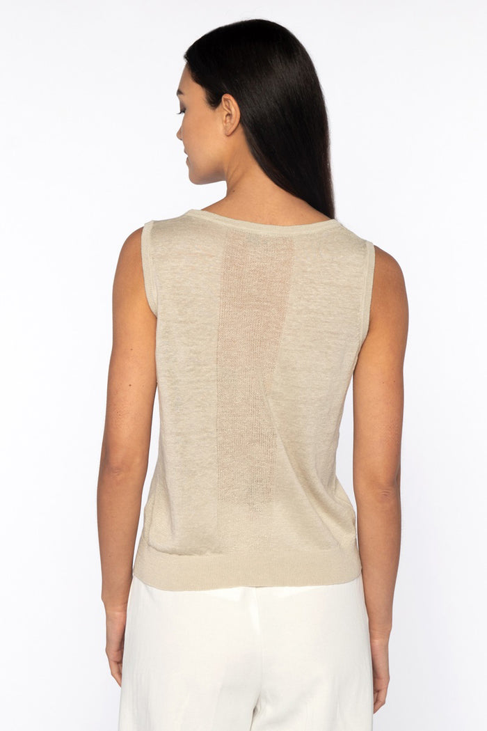 A woman with long dark hair models the KINROSS SLEEVELESS TANK IN LINEN, styled with white pants and hands in her pockets against a plain white background for a relaxed, everyday look.