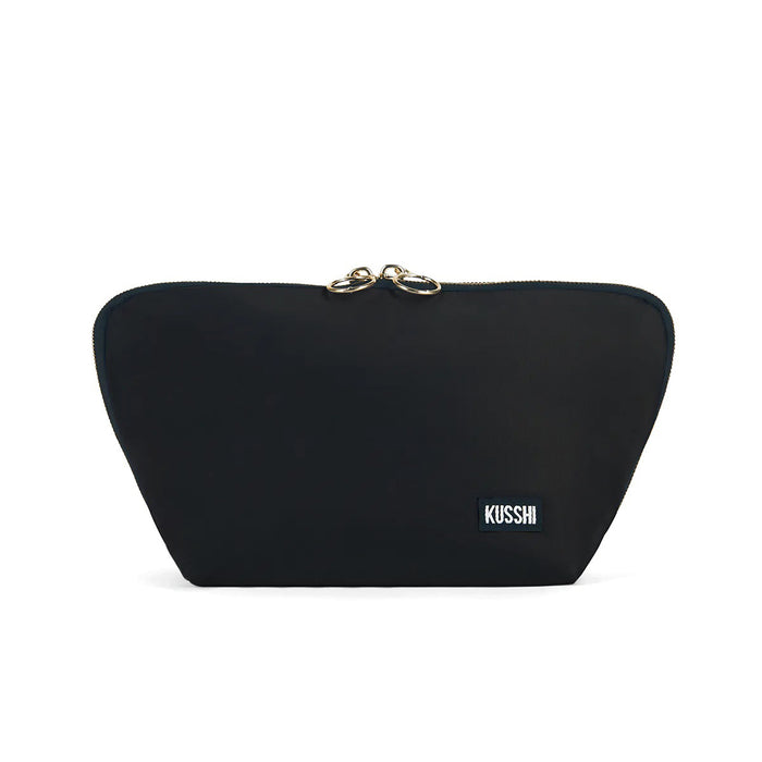 The KUSSHI - SIGNATURE MAKEUP BAG IN BLACK features a gold zipper and a small rectangular white and black "KUSSHI" logo patch on the lower right corner, displayed against a white background.