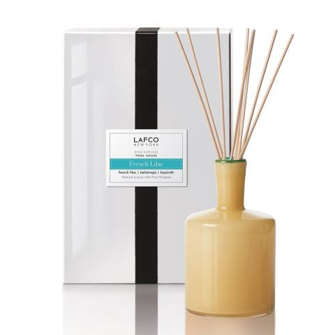 A yellow glass LAFCO Poolhouse Diffuser in French Lilac stands before a white box with a black ribbon, filling the air with hyacinth and heliotrope notes.
