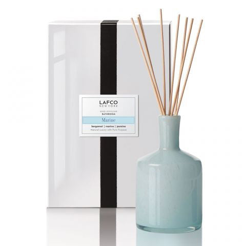 A light blue glass LAFCO - MARINE BATHROOM DIFFUSER with wooden reeds sits beside a white box featuring a black ribbon and label, offering refreshing marine water and uplifting bergamot scents.