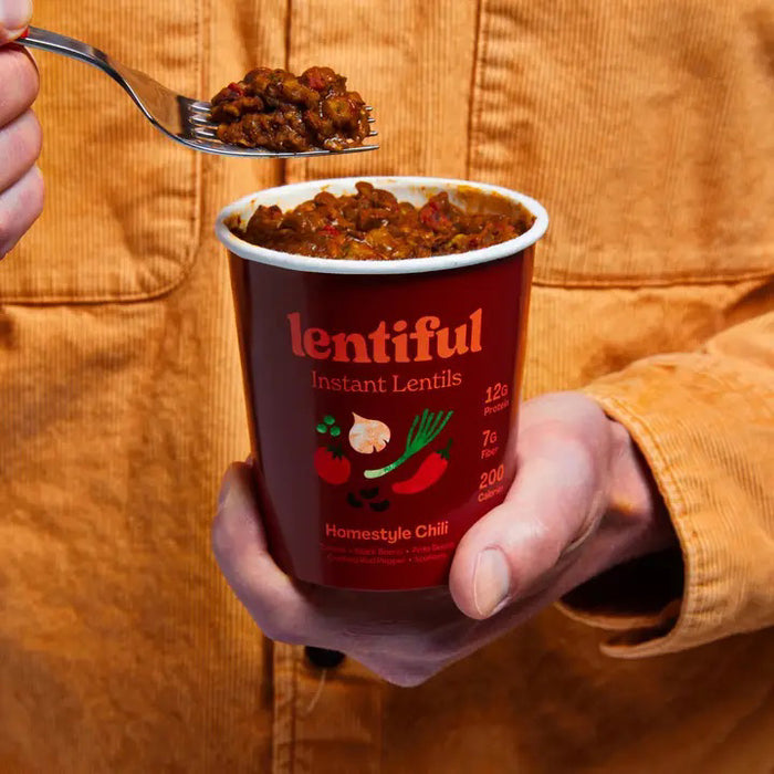 A green container of LENTIFUL - HOMESTYLE CHILI LENTILS with a dark green lid. The label features illustrations of green peppers, cilantro, and a beet. It highlights nutritional information: 12g protein, 7g fiber, 200 calories. Flavor: Mexican Green Chile, 2.65 oz. Shelf-stable for convenience.