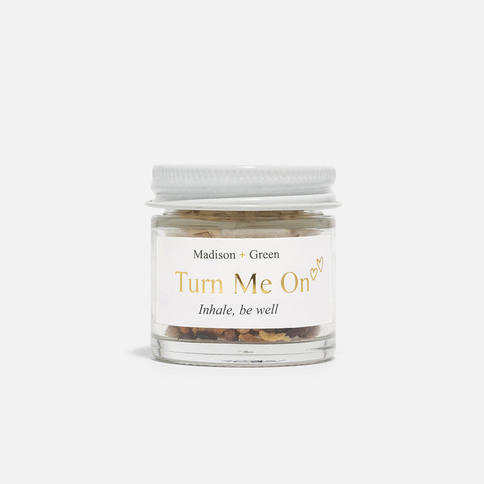 A young woman with long brown hair holds and smells the MADISON AND GREEN - TURN ME ON AROMATHERAPY INHALER by MADISON GREEN, savoring its essential oils in soft natural light against a plain background.