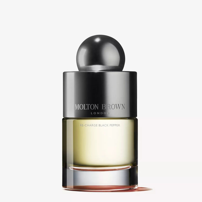 A 3.4 fl oz bottle of MOLTON BROWN Re-Charge Black Pepper Eau de Toilette features a silver rounded cap, clear glass with pale yellow liquid, and modern minimalist design on a white background, blending earthy vetiver and black pepper notes.
