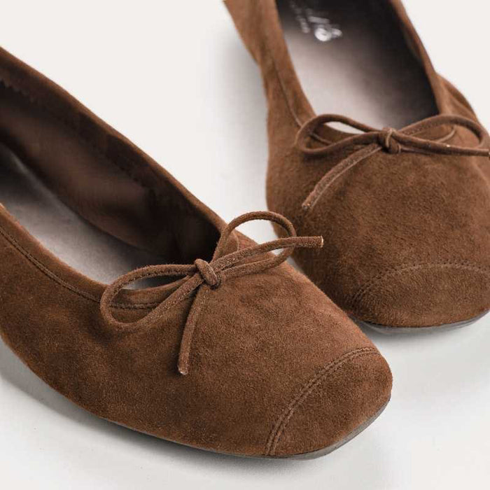 The REQINS HARMONY suede ballerina flats in Cacao, featuring delicate front bows, are shown against a plain light background.