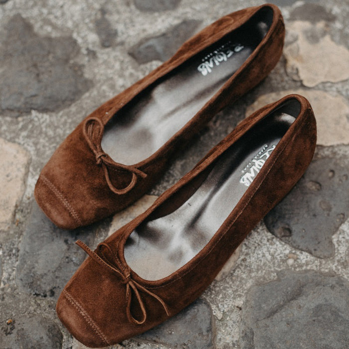 The REQINS HARMONY suede ballerina flats in Cacao, featuring delicate front bows, are shown against a plain light background.