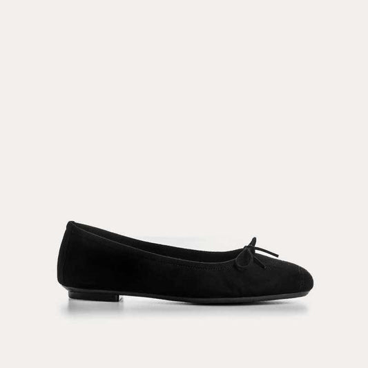 Wearing rolled-up blue jeans with REQINS - HARMONY SUEDE BALLERINA FLATS IN NOIR, featuring chic bow details—a timeless addition to any classic wardrobe.