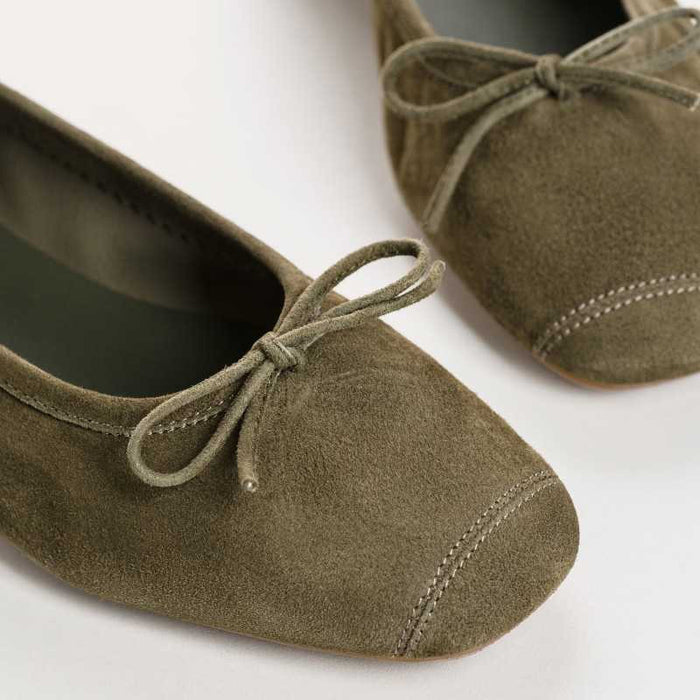 The REQINS - HARMONY suede ballerina flat in olive features a small bow on the toe, flat heel, and simple stitching, shown against a plain light background.