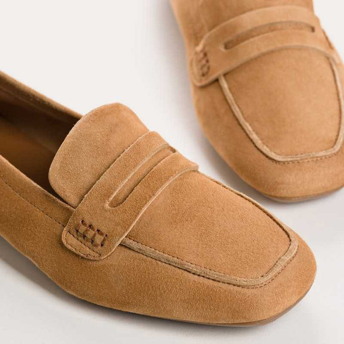 The REQINS - HEMA Suede Loafer in Camel features light brown suede, a low heel, rounded toe, decorative strap, and leather insole for comfort. Elegant finish shown in side profile on a plain white background.