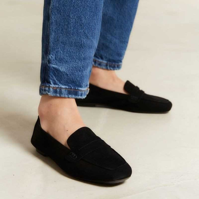 The REQINS HEMA Suede Loafer in Noir features a classic black silhouette, low heel, leather insole, and decorative front strap, shown against a plain light background.