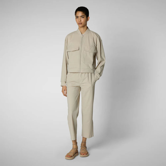 A person with shoulder-length hair and a neutral expression wears a white long-sleeve shirt, SAVE THE DUCK MILAN PULL ON PANT in black wrinkle-free fabric, and black slip-on shoes. Their hands rest at their sides against a plain background.