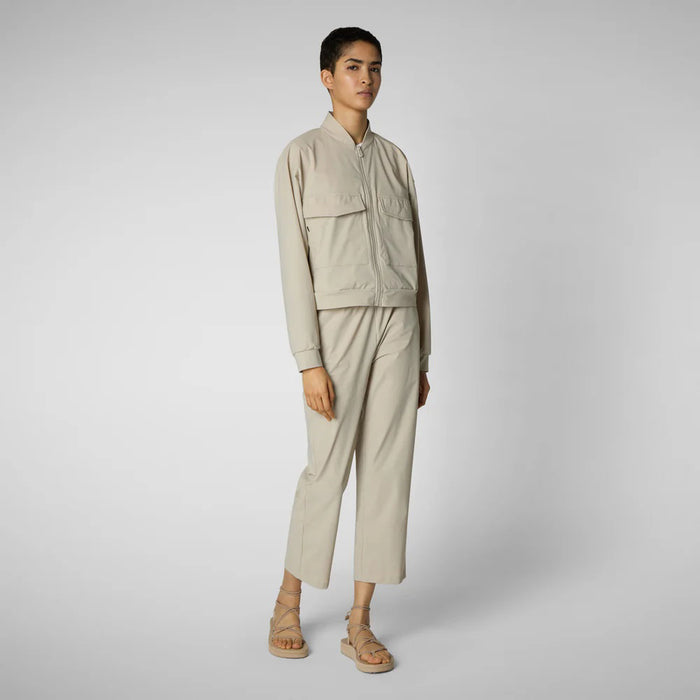 A person with shoulder-length hair and a neutral expression wears a white long-sleeve shirt, SAVE THE DUCK MILAN PULL ON PANT in black wrinkle-free fabric, and black slip-on shoes. Their hands rest at their sides against a plain background.