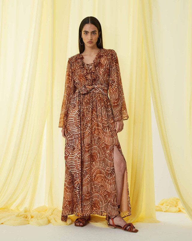 The SFIZIO - RUST PRINT RUFFLED DRESS by SFIZIO is a long-sleeved, floor-length Italian dress in airy viscose creponne with a cinched waist, ruffled neckline, and abstract brown/beige print on lightweight, semi-sheer fabric.