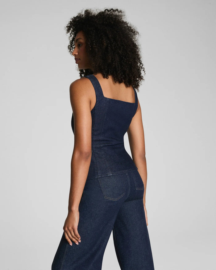 A woman with curly hair models the SPANX DENIM TAILORED VEST, posing confidently against a plain light gray background.