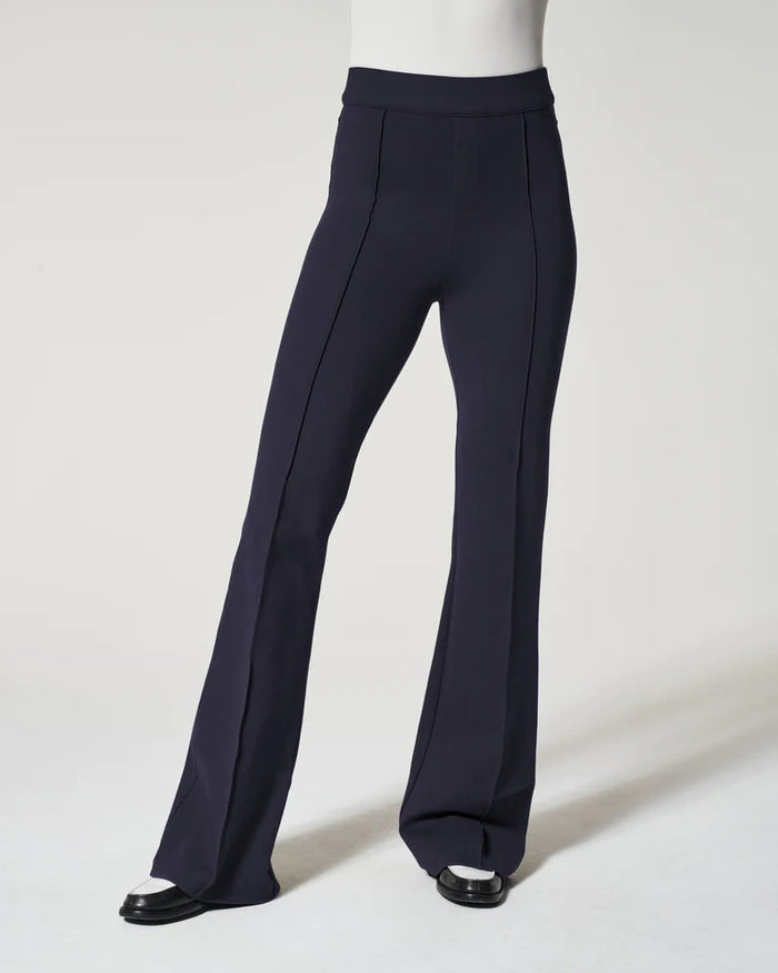 A woman models the SPANX Perfect Pant High Rise Flare in navy with a matching blazer, white fitted top, and black-and-white shoes, highlighting the sleek pull-on design from SPANX against a plain light background.