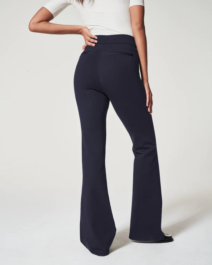 A woman models the SPANX Perfect Pant High Rise Flare in navy with a matching blazer, white fitted top, and black-and-white shoes, highlighting the sleek pull-on design from SPANX against a plain light background.
