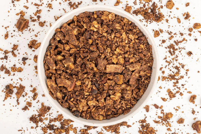 A black and gold pouch labeled "STRUESLI - CACO + COFFE GRANOLA" from STRUESLI showcases its grain-free, unsweetened, prebiotic, plant-based granola made in small batches, set against a plain background.