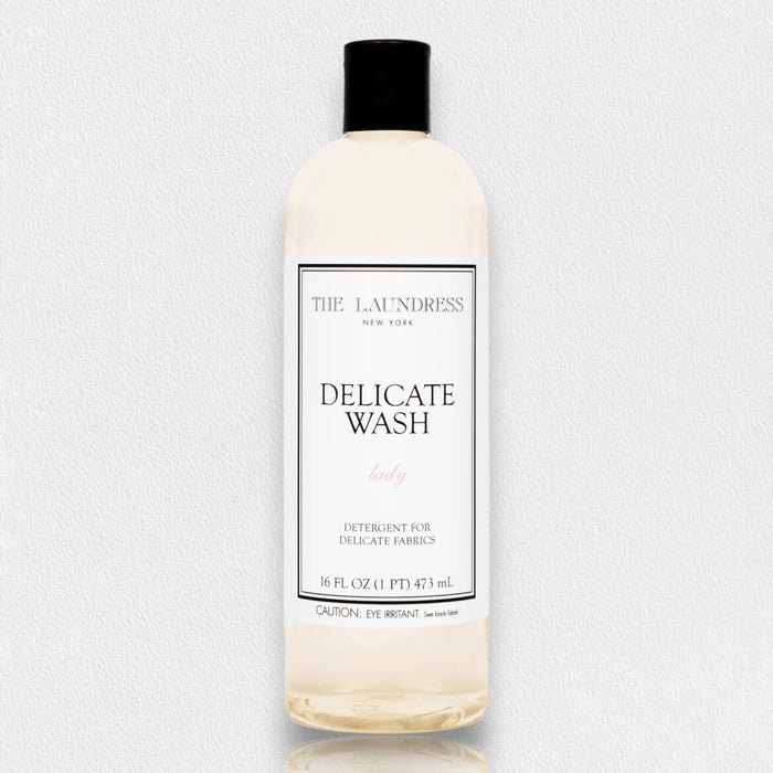 A clear 16oz (473ml) bottle of THE LAUNDRESS - DELICATE WASH gentle detergent with a black cap, featuring a white label with black and pink text; ideal by THE LAUNDRESS for washing delicate fabrics.