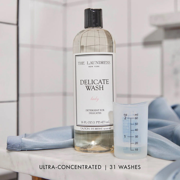 A clear 16oz (473ml) bottle of THE LAUNDRESS - DELICATE WASH gentle detergent with a black cap, featuring a white label with black and pink text; ideal by THE LAUNDRESS for washing delicate fabrics.
