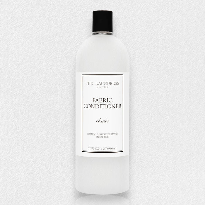 THE LAUNDRESS - FABRIC CONDITIONER 32OZ is a plant-derived fabric softener that helps reduce static. It comes in a clear plastic bottle with a black cap and contains 32 fl oz (946 ml).