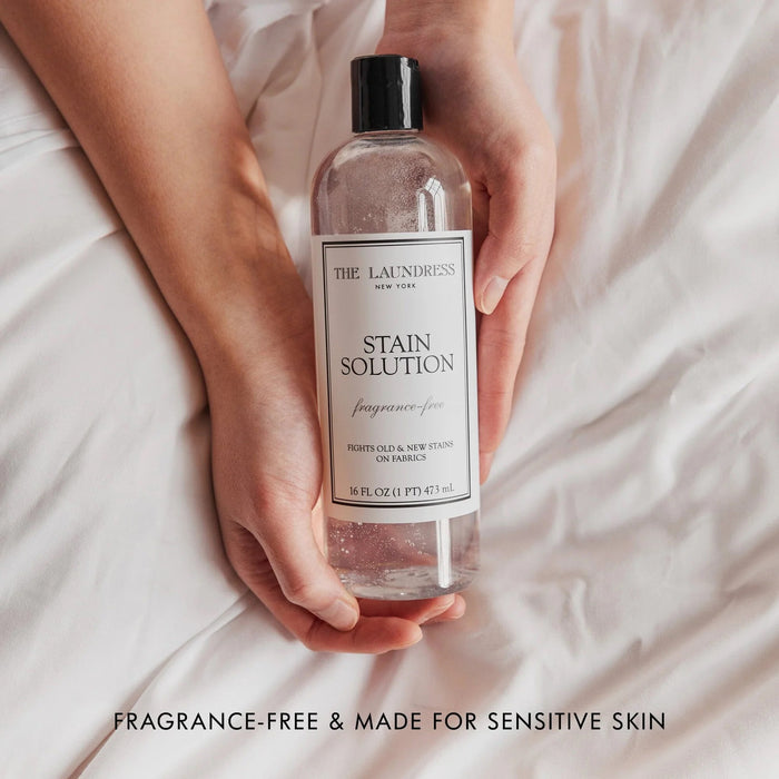 A clear bottle of THE LAUNDRESS - STAIN SOLUTION 16OZ enzyme cleaner, fragrance-free, removes old and new stains from fabrics.