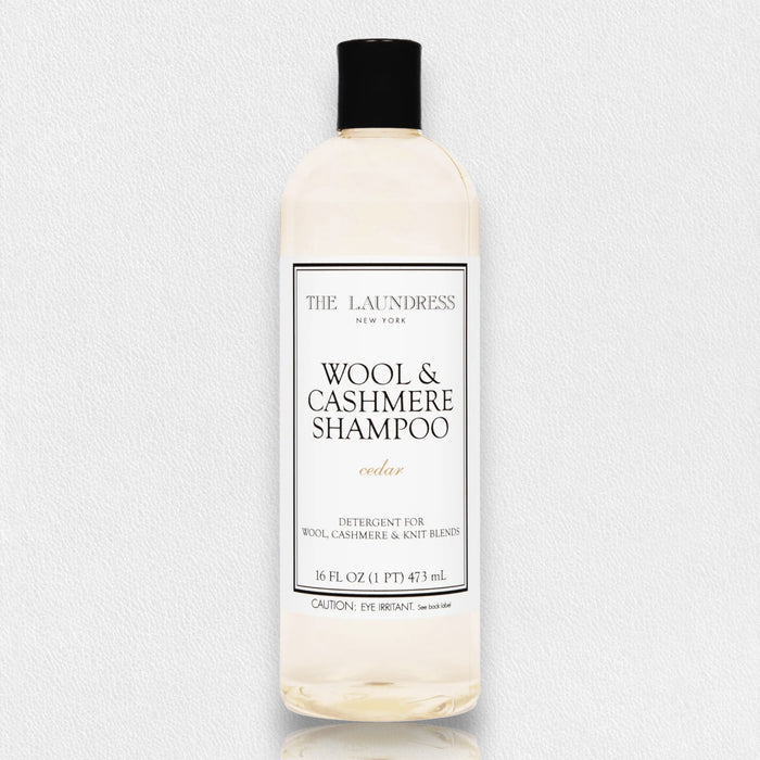 A 16oz clear plastic bottle of THE LAUNDRESS WOOL AND CASHMERE SHAMPOO, cedar-scented, with a white label and black text. This enzyme-free detergent is perfect for gently cleaning wool and knit blends.