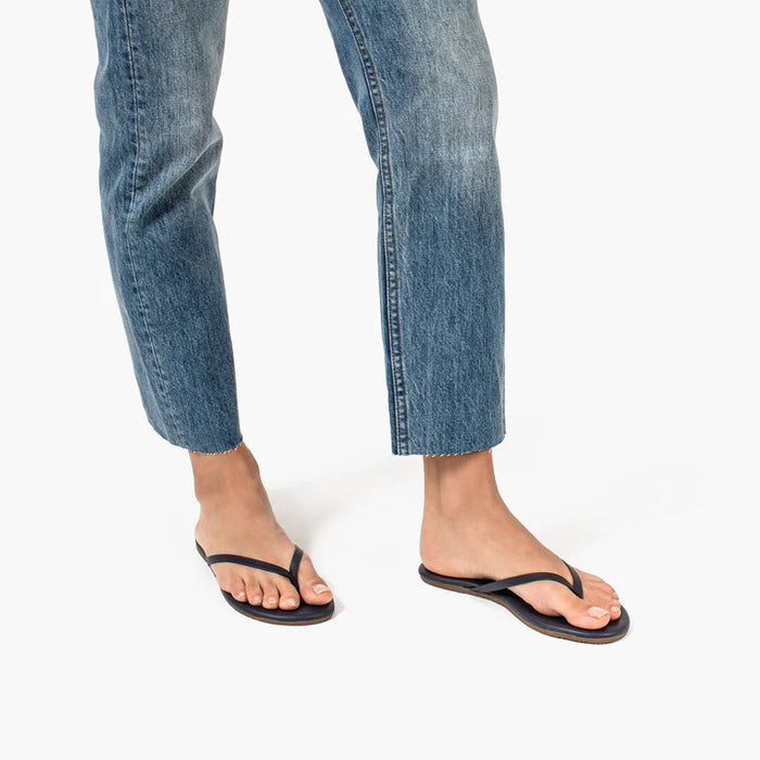 The TKEES - LILY LINER SLIPPER TWILIGHT by TKEES INC are simple dark flip-flops with thin straps and cushioned insoles, featuring the brand name printed on each insole and displayed on a white background.