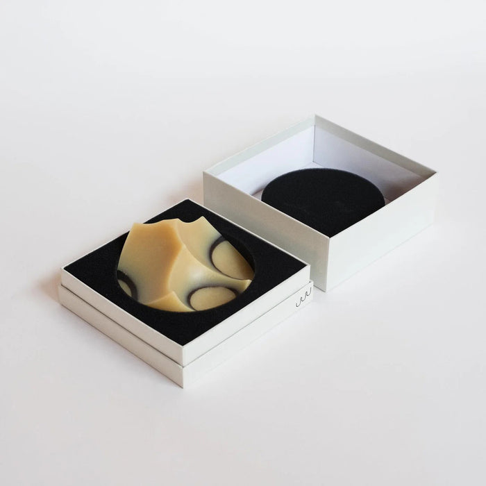 The UME STUDIO UME - CEDAR SANDALWOOD ERODE SOAP, featuring curved geometric shapes in beige and black, rests on a round black dish against a white background, showcasing its botanical formula with essential oils.