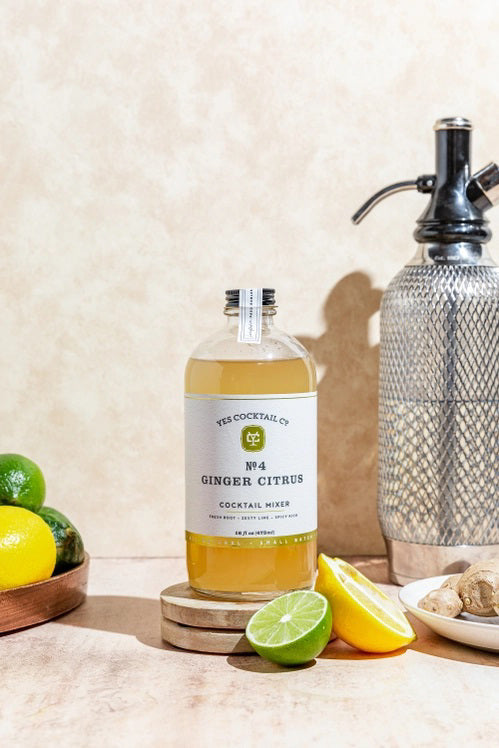 A clear glass 16 fl oz (473 ml) bottle of YES COCKTAIL CO - GINGER CITRUS COCKTAIL MIXER with a white label, green accents, and black text. The pale yellow mixer delivers a zesty ginger citrus kick—perfect for mule cocktails.