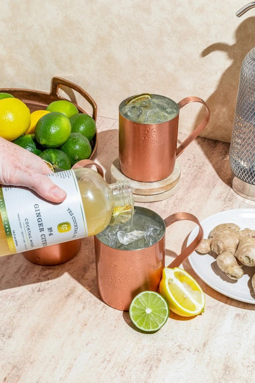 A clear glass 16 fl oz (473 ml) bottle of YES COCKTAIL CO - GINGER CITRUS COCKTAIL MIXER with a white label, green accents, and black text. The pale yellow mixer delivers a zesty ginger citrus kick—perfect for mule cocktails.